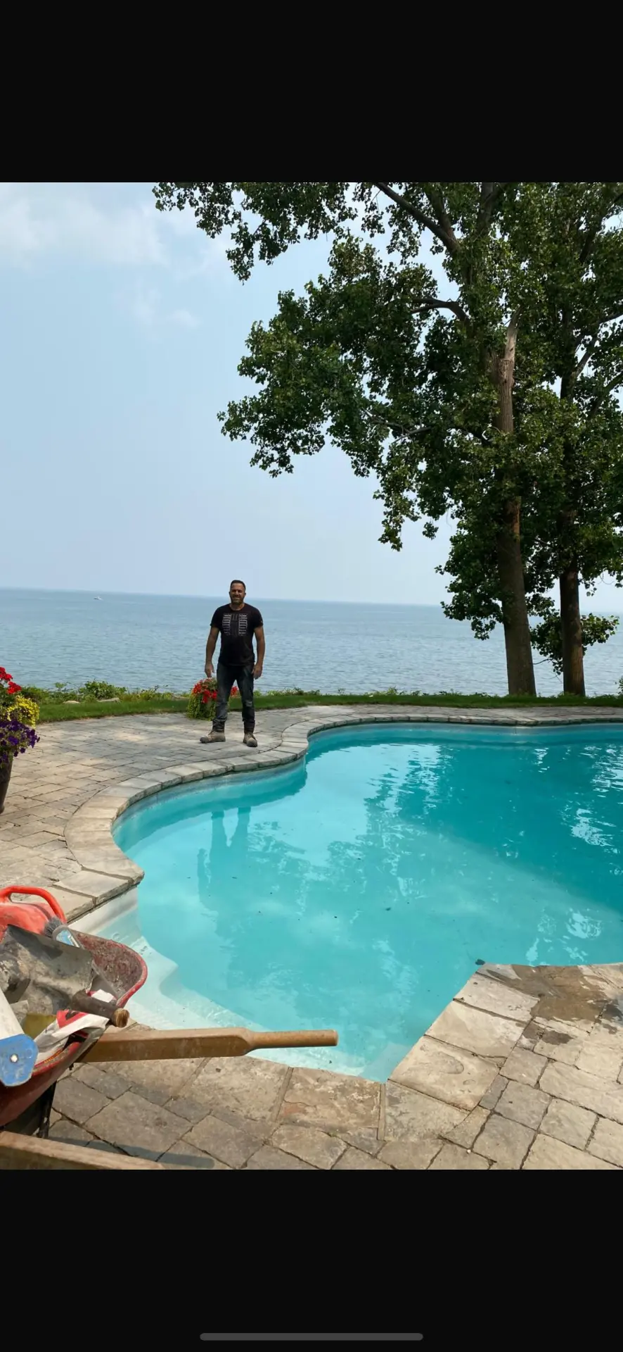 Karmi Landscaping owner beside a completed lakeside pool with natural stone decking
